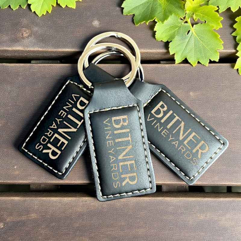 Custom engraved keychains and bottle openers featuring Bitner Vineyards branding on a wooden surface.