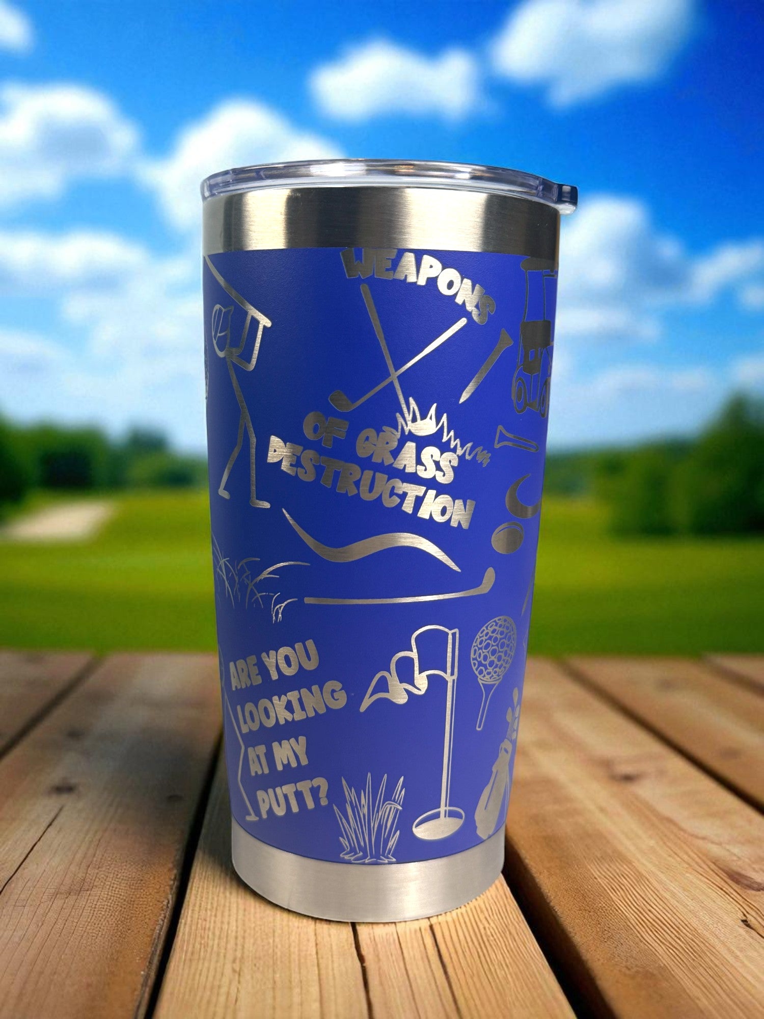 Blue tumbler with golf-themed design on a wooden surface with a blurred outdoor background
