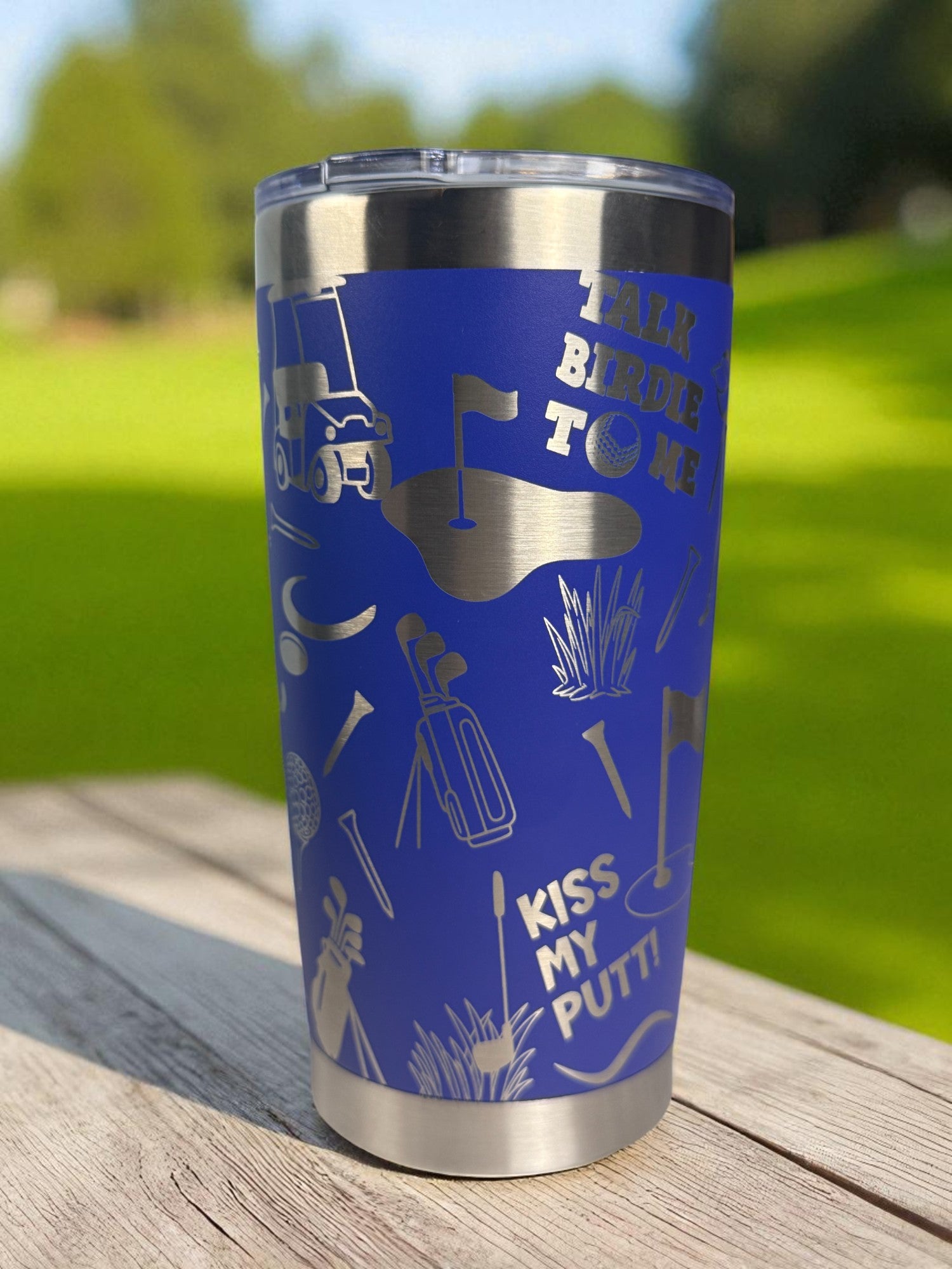 Blue tumbler with golf-themed designs on a wooden surface with a grassy background