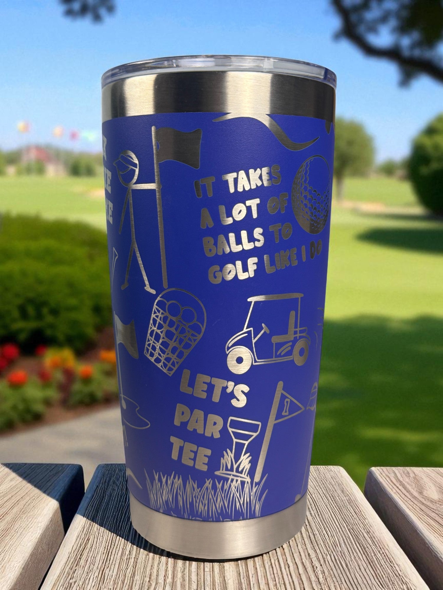 Blue tumbler with golf-themed design on a wooden surface with a golf course background