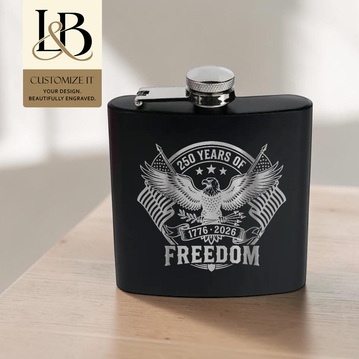 Black flask with a silver eagle-and-Freedom design and gold brand badge on a pale table.