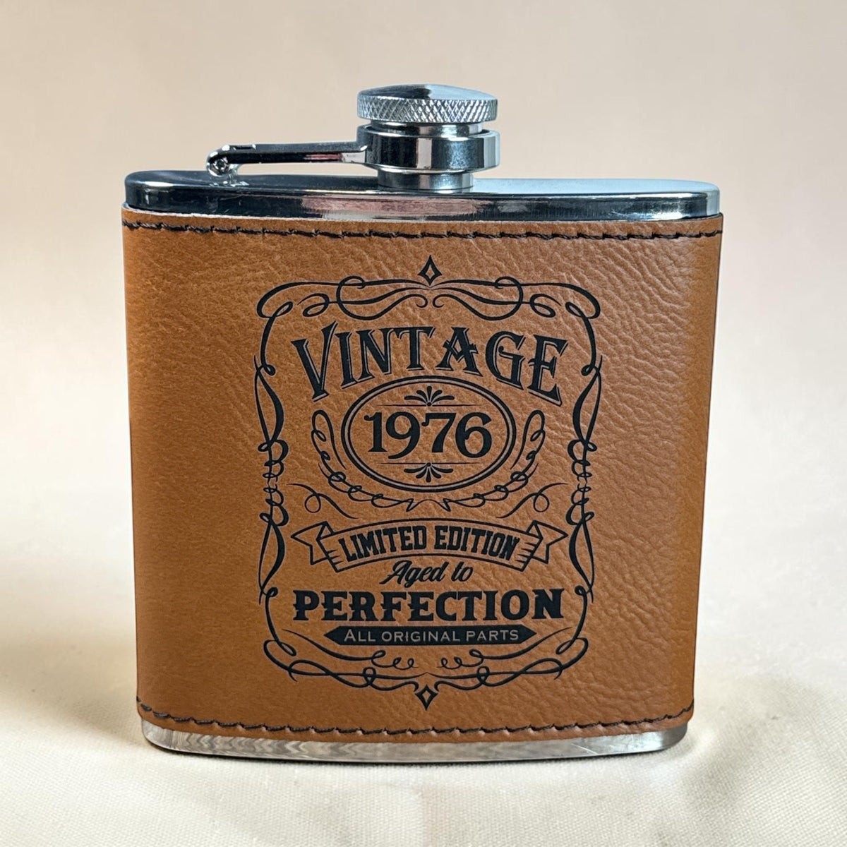 Brown Vintage 1976 flask with Aged to Perfection engraving and a gold brand badge, front view.