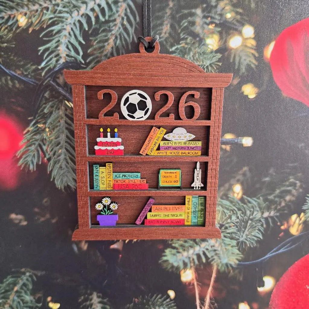 2026 wooden bookshelf ornament hanging on a Christmas tree with holiday lights