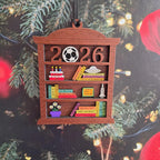 2026 wooden bookshelf ornament hanging on a Christmas tree with holiday lights