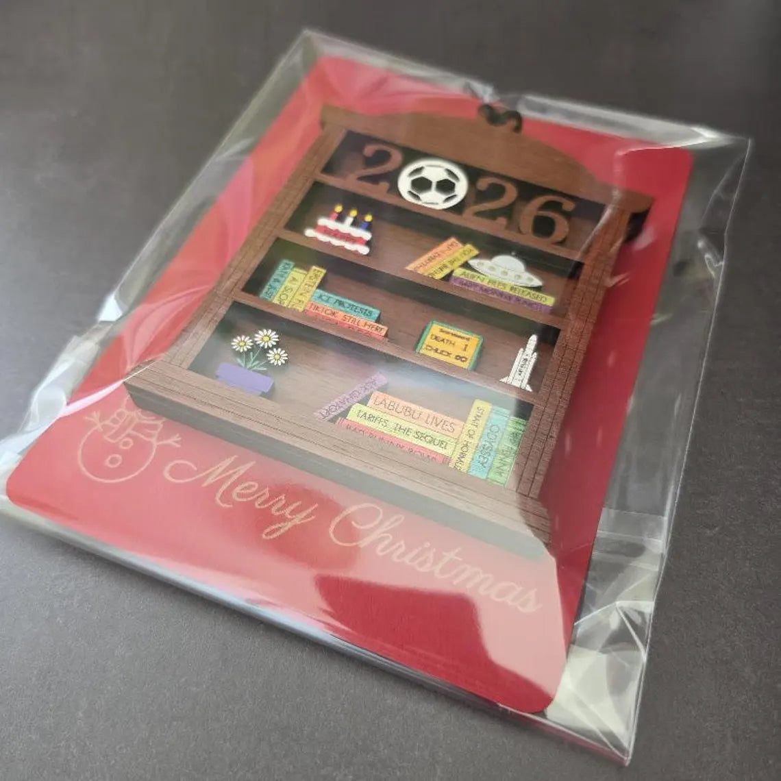 2026 time capsule ornament packaged in clear sleeve with red Merry Christmas backing card