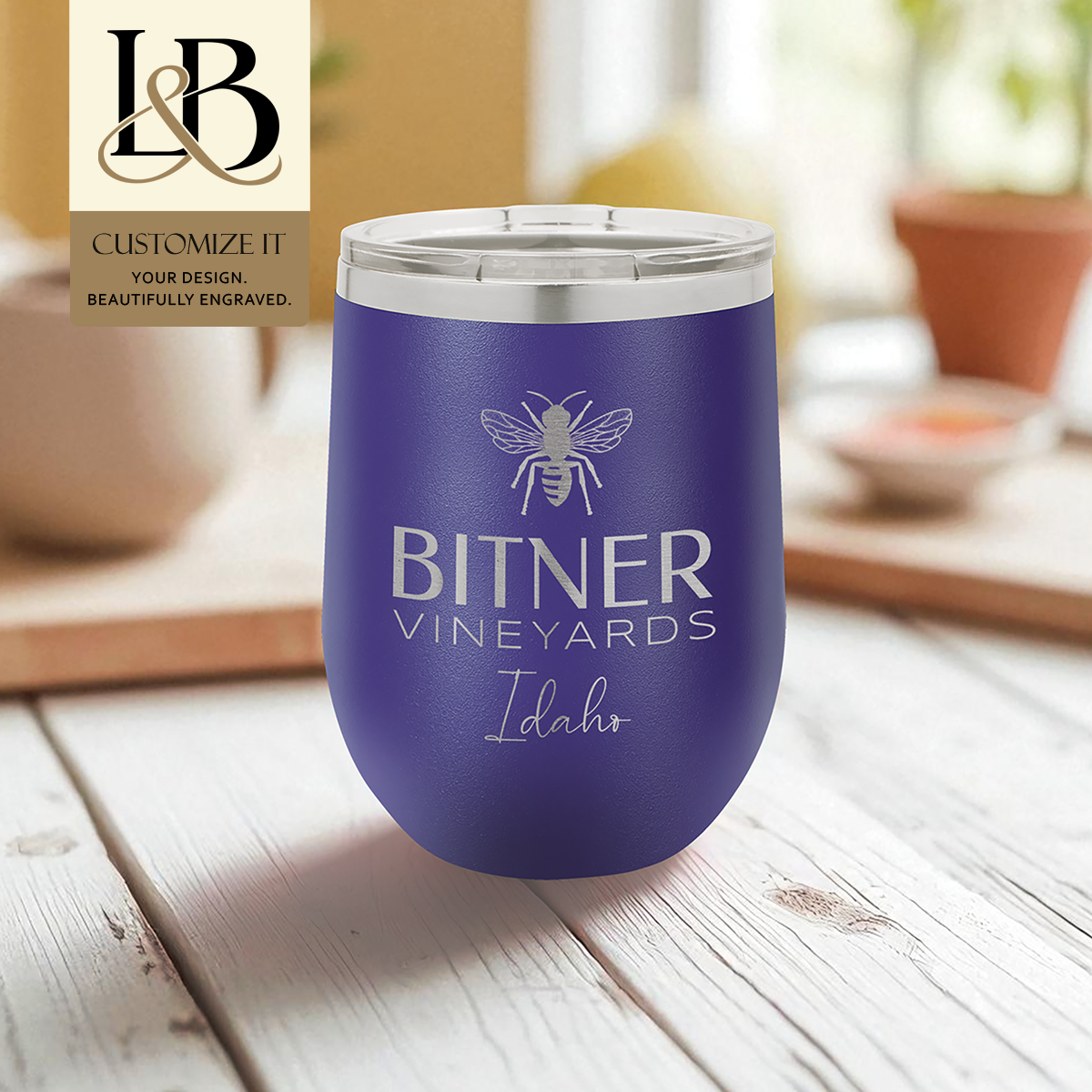 Purple Bitner Vineyards wine tumbler with engraved logo and a gold brand badge in a cafe setting.