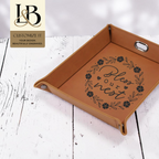 Rawhide rectangular tray with an engraved floral saying and gold brand badge on pale wood.