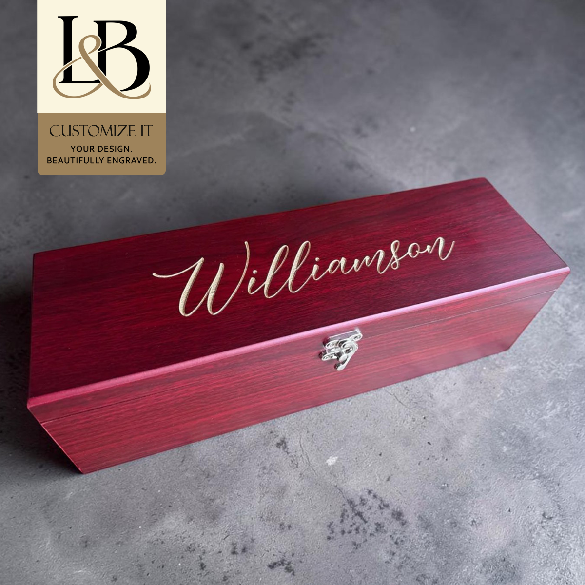 Red Williamson personalized wine gift box with silver latch and a gold brand badge on gray stone.